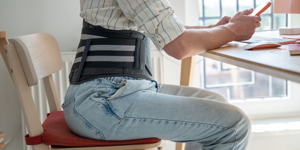 Man wearing a back brace while sitting down at desk